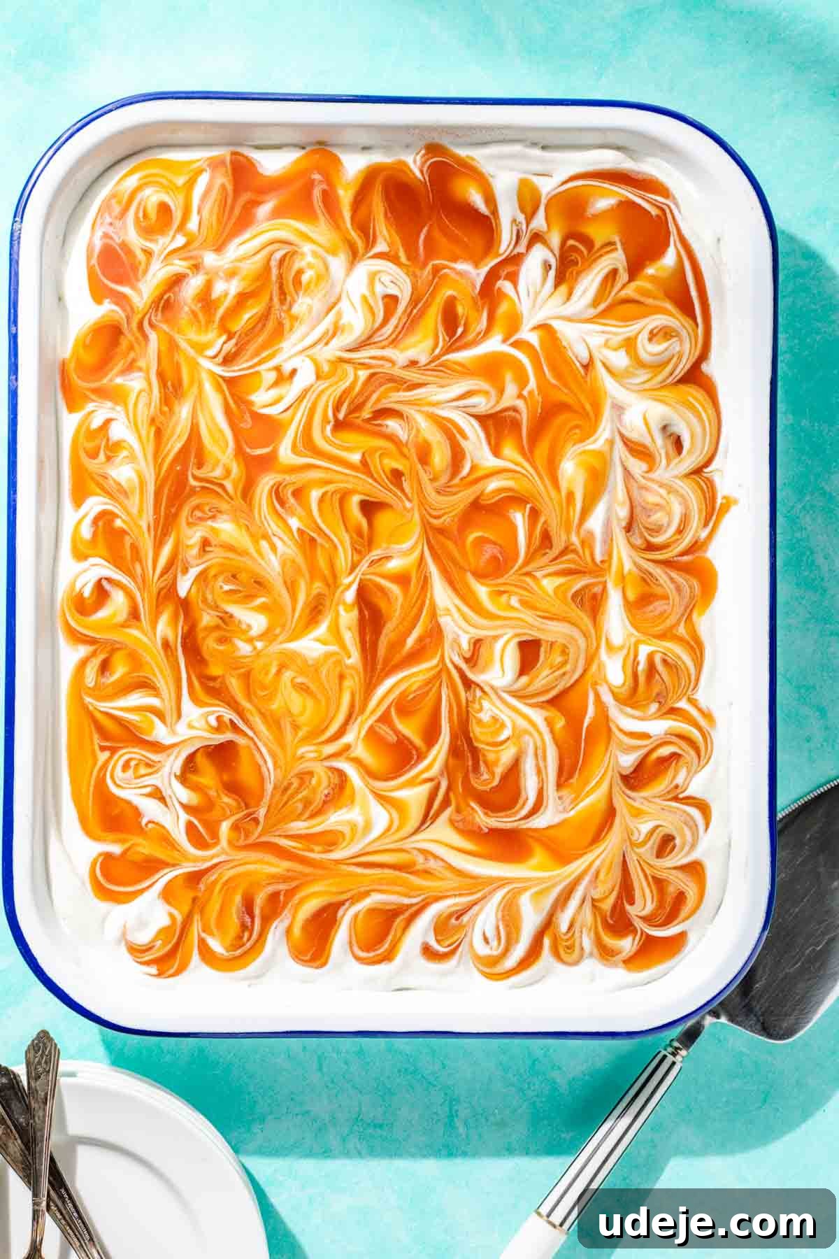 Heavenly Turkish Milk Cake 2 Turkish Tres Leches cake in a white baking pan on a blue background with a silver cake server and white plates and utensils on the sides