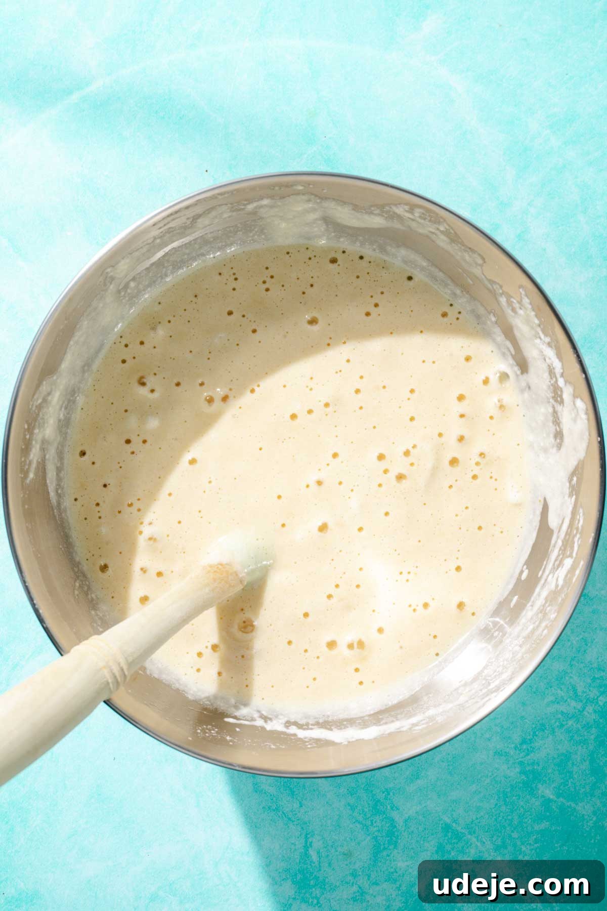 Heavenly Turkish Milk Cake 12 Cake batter mixed together with a blue spatula in a metal bowl on a blue background