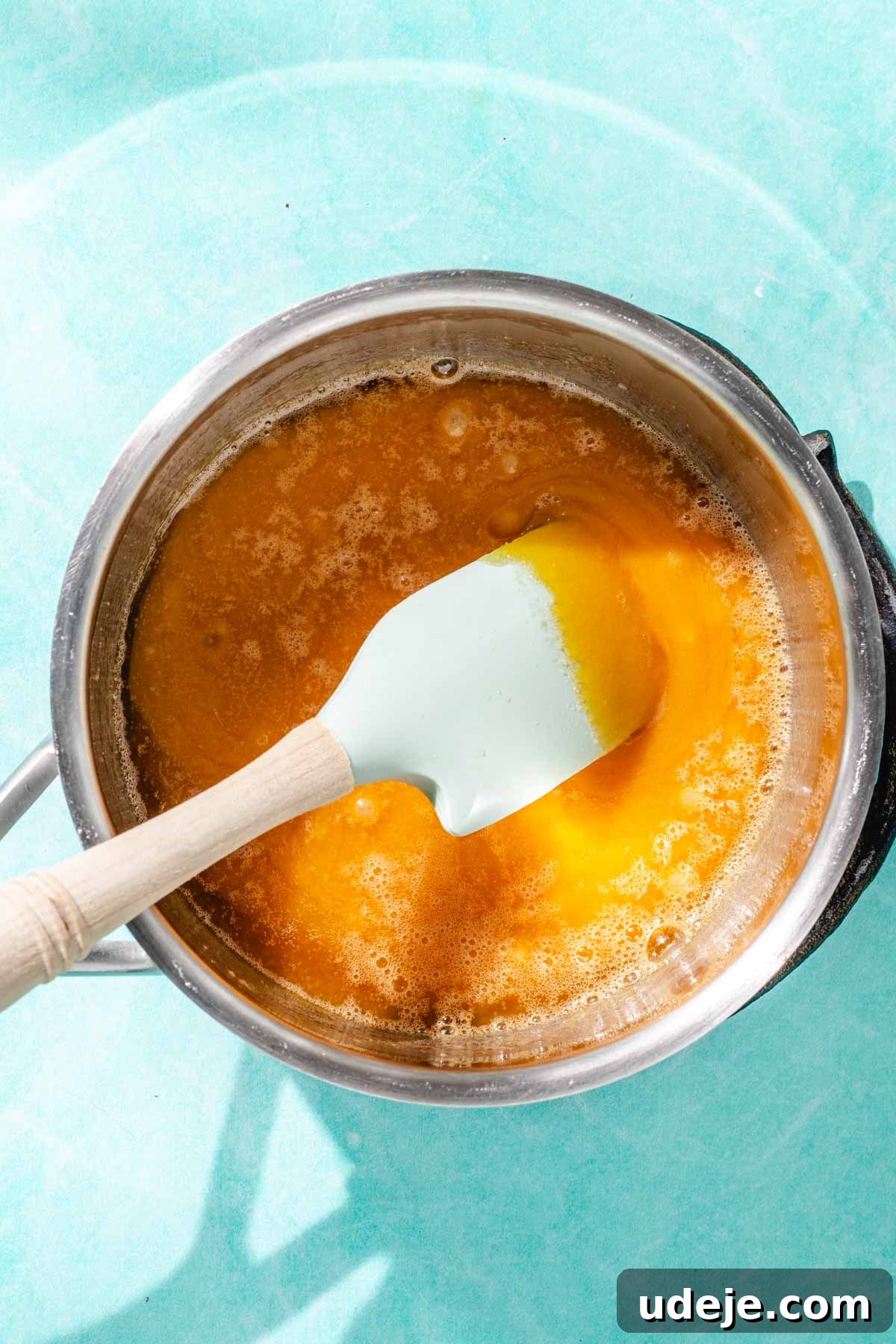 Heavenly Turkish Milk Cake 15 Sugar turning into caramel with a blue spatula in a metal saucepan on a blue background