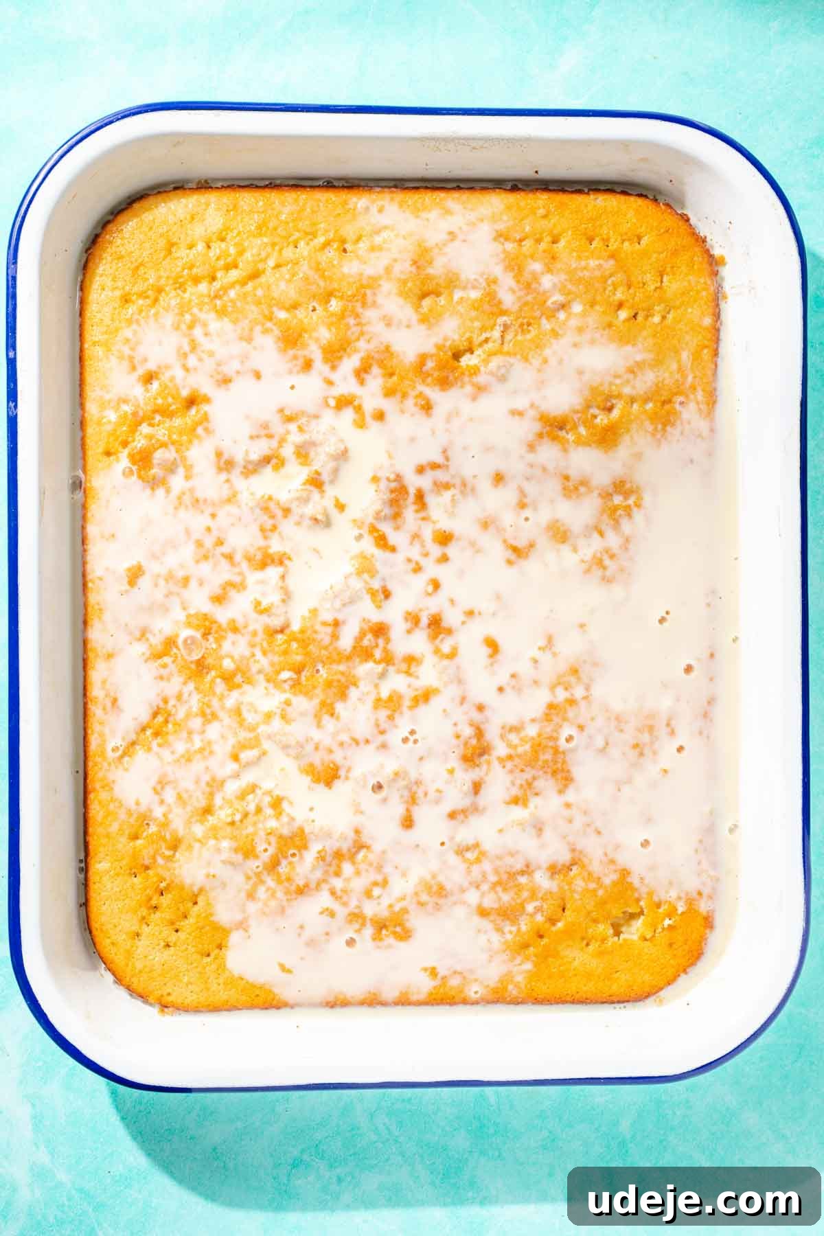 Heavenly Turkish Milk Cake 22 Milk mixture soaking into cake in a white baking pan on a blue background