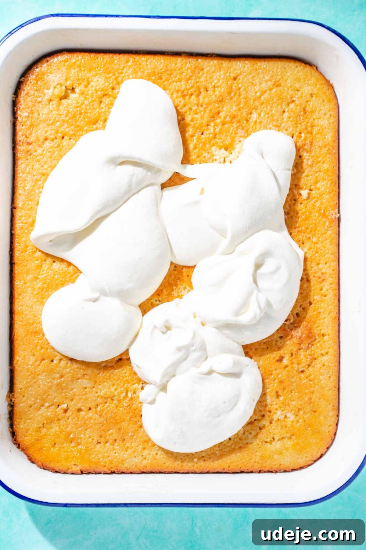Heavenly Turkish Milk Cake 24 Whipping cream dolloped on soaked milk cake in a white baking pan on a blue background