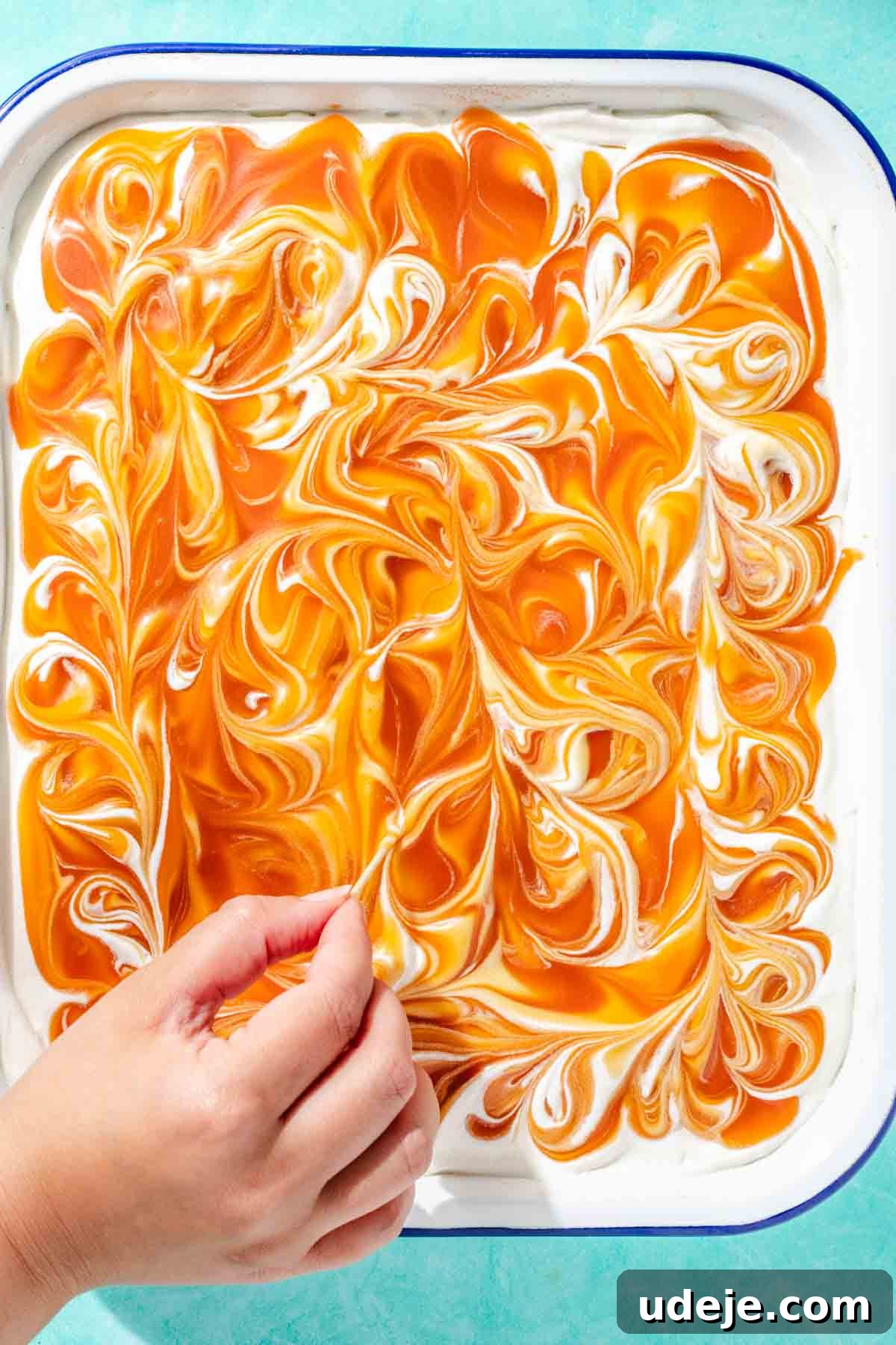 Heavenly Turkish Milk Cake 27 Decorative swirls being swirled into caramel sauce on cake in white baking pan on a blue background