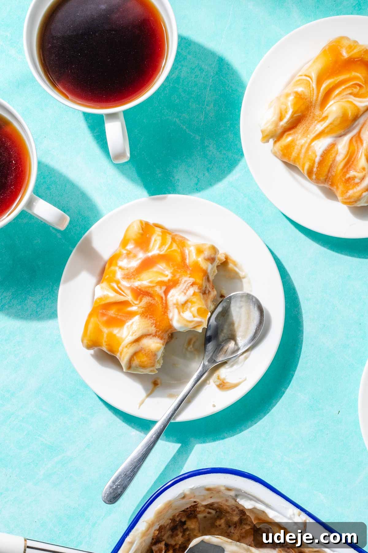 Heavenly Turkish Milk Cake 30 Slices of turkish tresh leches on white plates with one having a few bites eaten with a spoon at the side, cups of coffee and white pan of tres leches at the side on a blue background