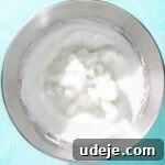 Large metal bowl with fluffy whisked egg whites on a blue background