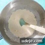 Whisked egg mixture in a metal mixing bowl with a blue spatula on a blue background