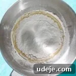 Flour added to whisked egg mixture in metal mixing bowl on a blue background