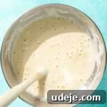 Cake batter mixed together with a blue spatula in a metal bowl on a blue background