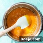 Sugar turning into caramel with a blue spatula in a metal saucepan on a blue background