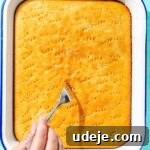Holes being poked into cake by a fork in a white baking pan on a blue background