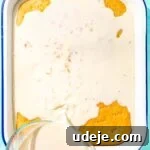 Milk mixture being poured from a glass measuring cup over cake in a white baking pan on a blue background
