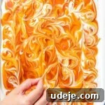 Decorative swirls being swirled into caramel sauce on cake in white baking pan on a blue background