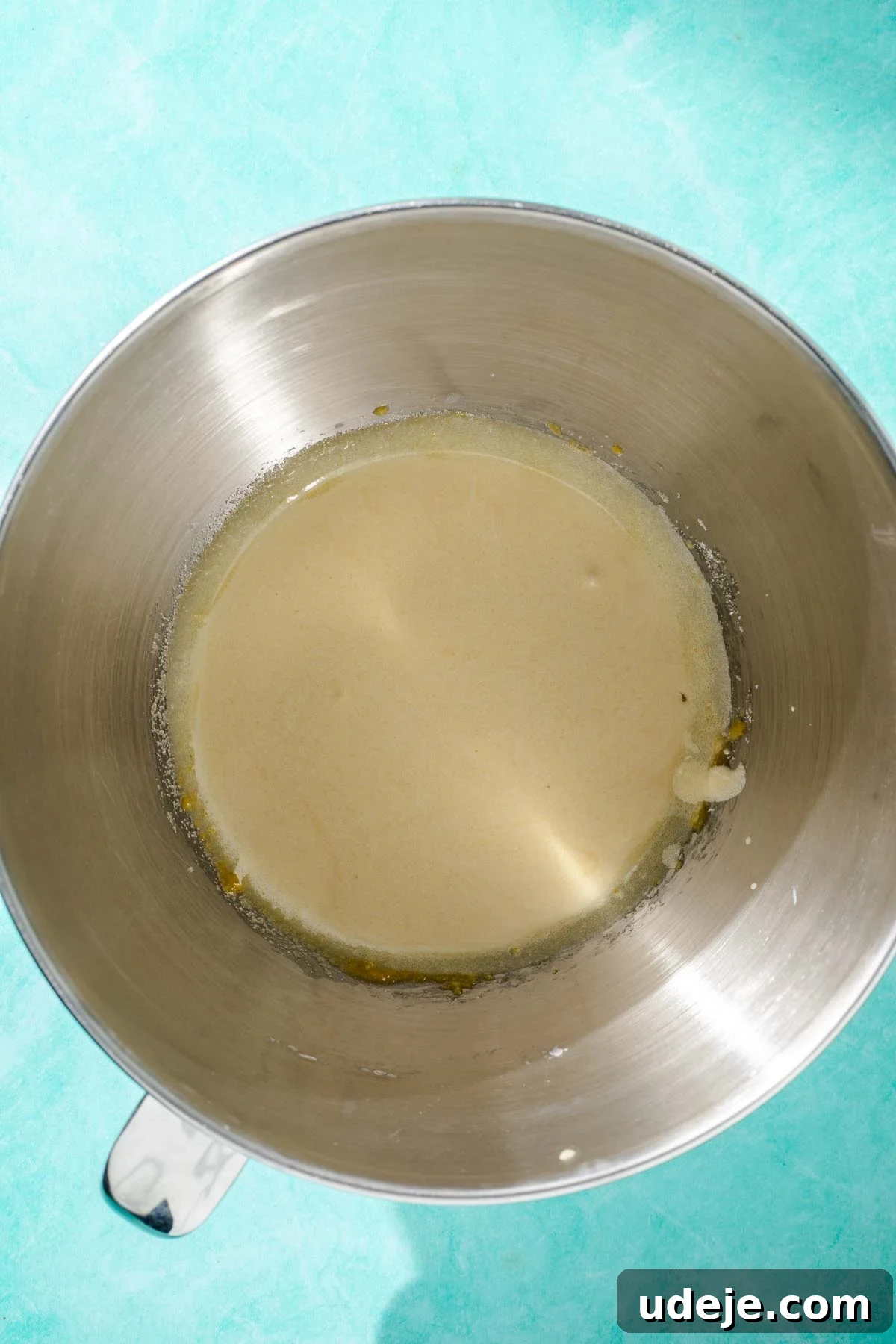 Heavenly Turkish Milk Cake 6 Metal mixing bowl with light coloured whisked egg yolks on a blue background