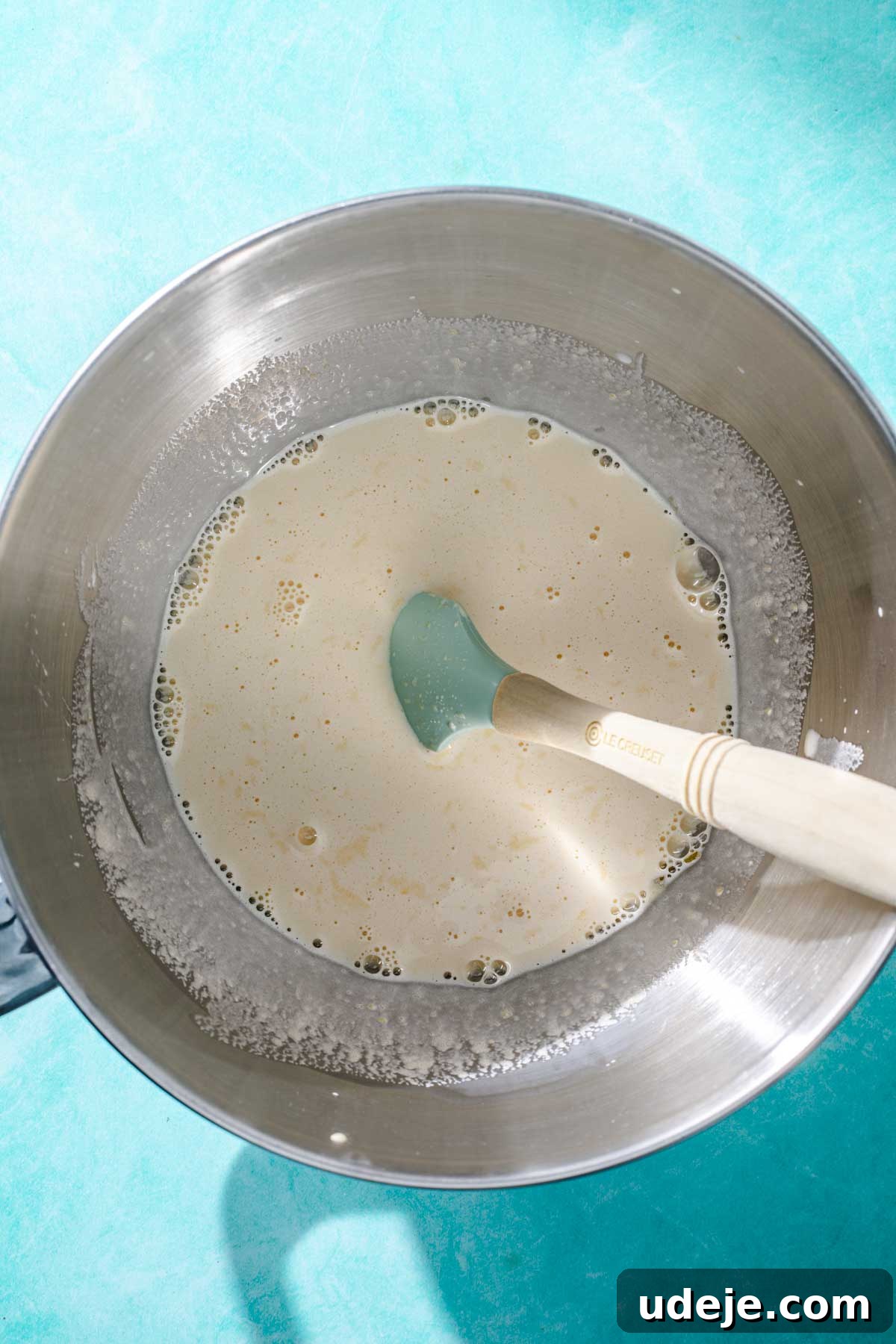 Heavenly Turkish Milk Cake 8 Whisked egg mixture in a metal mixing bowl with a blue spatula on a blue background