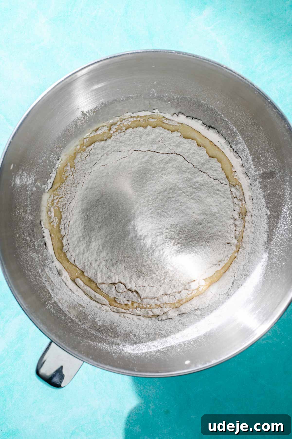 Heavenly Turkish Milk Cake 9 Flour added to whisked egg mixture in metal mixing bowl on a blue background