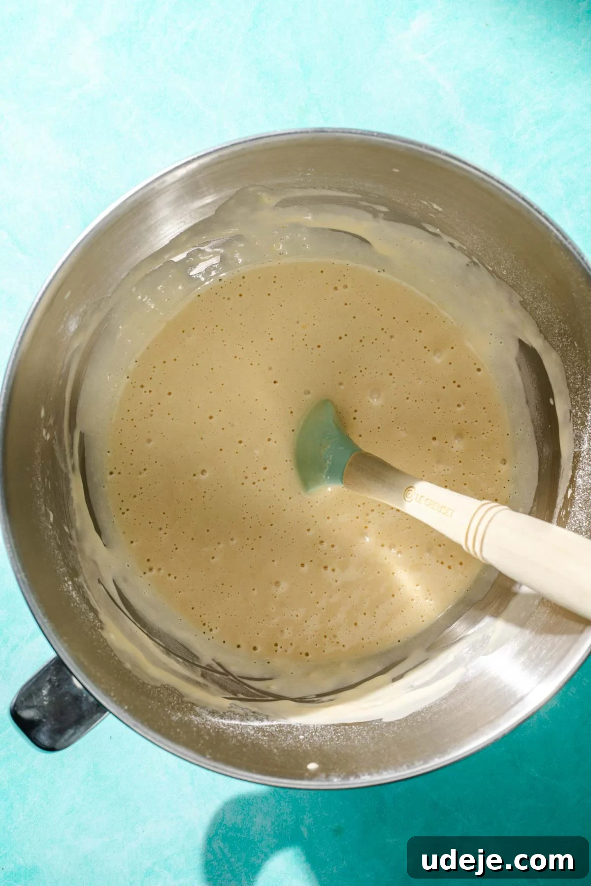Heavenly Turkish Milk Cake 10 Mixed cake batter in a metal mixing bowl with a blue spatula on a blue background