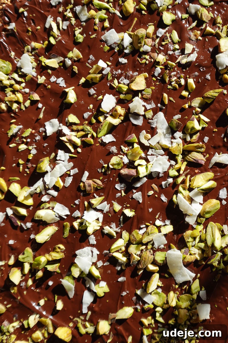 Wholesome Chocolate Quinoa Crunch Bark 5 Chocolate quinoa bark topped with shredded coconut, chopped pistachios, and flaky sea salt, presented on parchment paper just before freezing, showcasing the beautiful toppings.