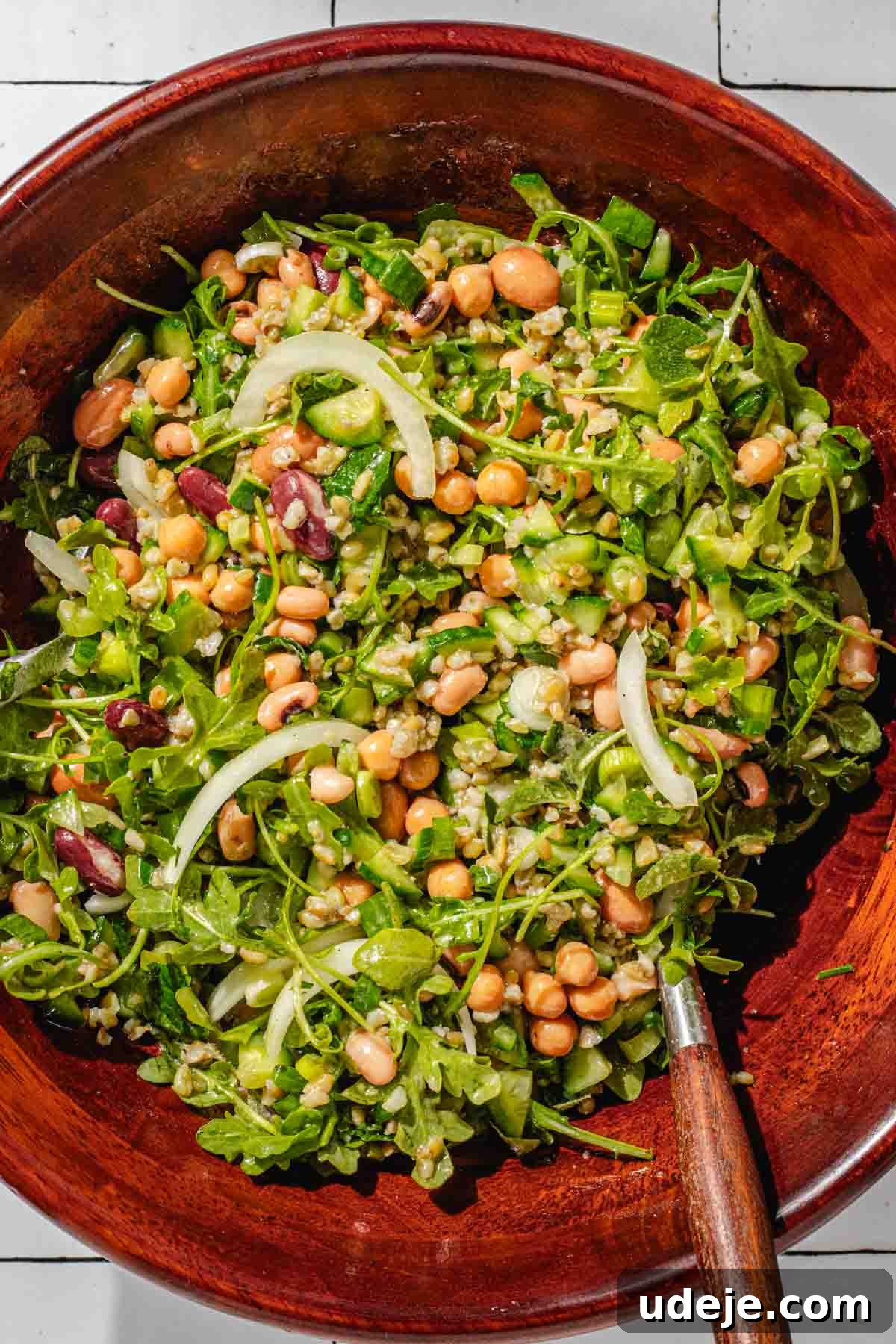 Silky Freekeh Bean Fiesta 11 A large wooden salad bowl with Freekeh Salad inside. The salad includes arugula, chopped cucumber, sliced onions, beans, cooked freekeh, and chopped parsley.