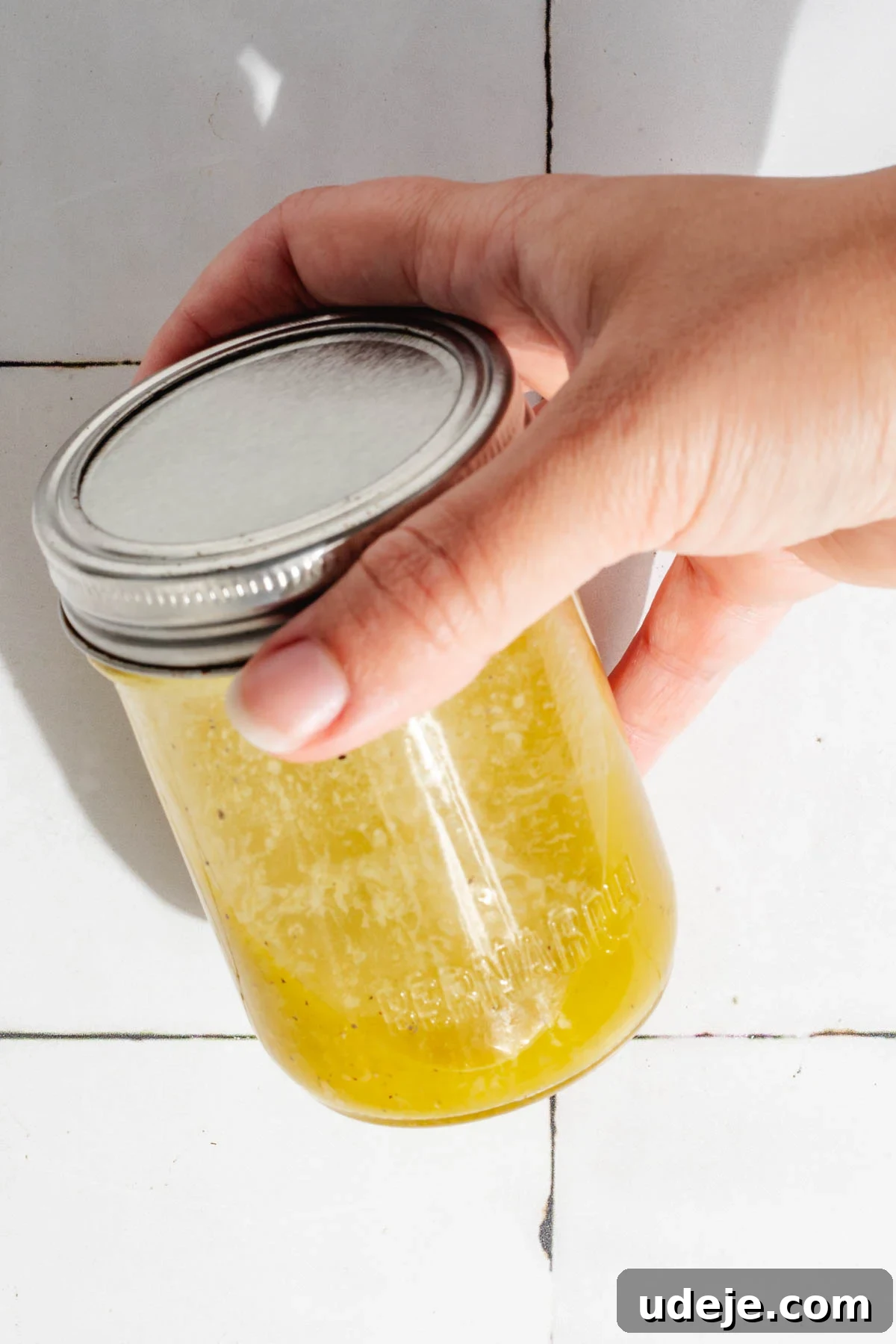Silky Freekeh Bean Fiesta 9 A honey mustard dressing in a small glass jar with a silver lid, being shaken
