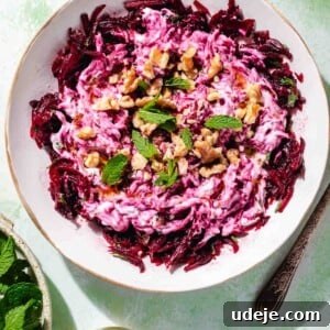 Vibrant Beetroot Yogurt Salad 10 Turkish beet salad garnished with walnuts and mint in a white salad bowl on a green background with a fork at the side, a small beige bowl with mint leaves and a small oil dispenser with olive oil