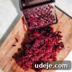 Vibrant Beetroot Yogurt Salad 12 Grated beet with a metal grater on a wooden cutting board on a white background