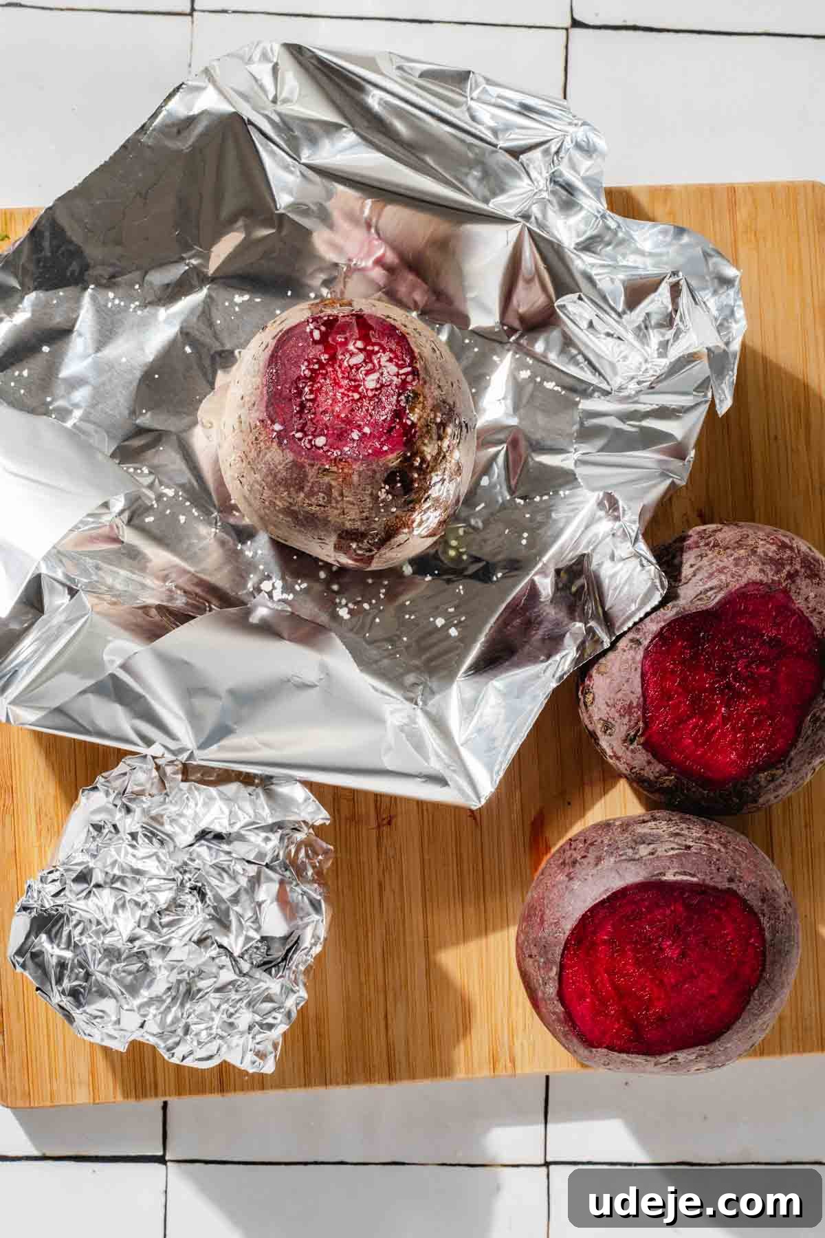 Vibrant Beetroot Yogurt Salad 4 Beets with the tops cut off and one placed in foil and sprinkled with salt on a wooden cutting board on a white tiled background