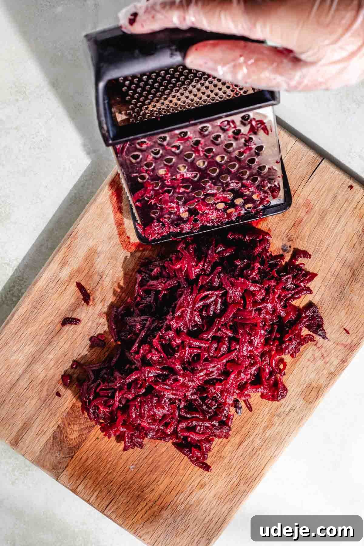 Vibrant Beetroot Yogurt Salad 5 Grated beet with a metal grater on a wooden cutting board on a white background