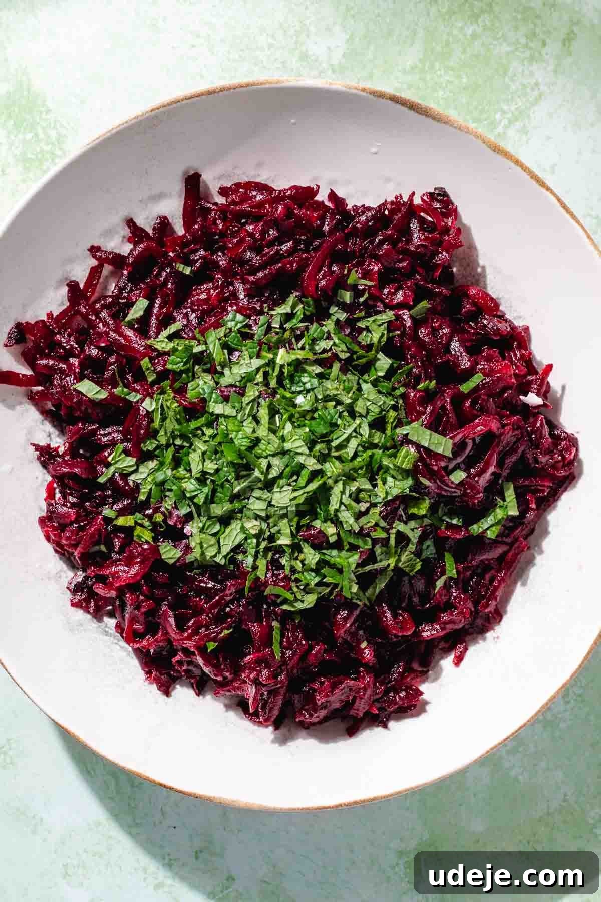 Vibrant Beetroot Yogurt Salad 6 Grated beet in a white salad bowl with chopped mint on top on a green background