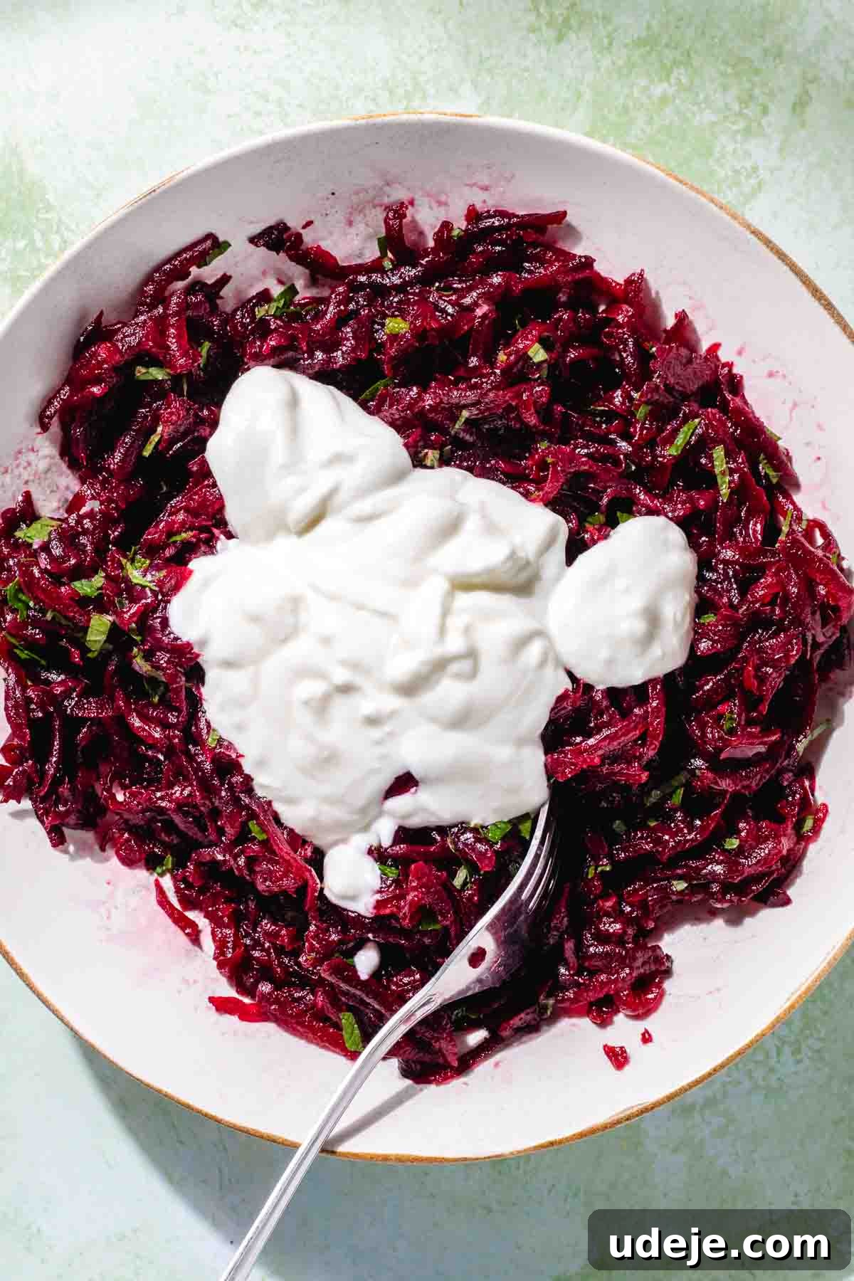 Vibrant Beetroot Yogurt Salad 7 Grated beet with mint and yogurt on top in a white salad bowl with a fork on a green background