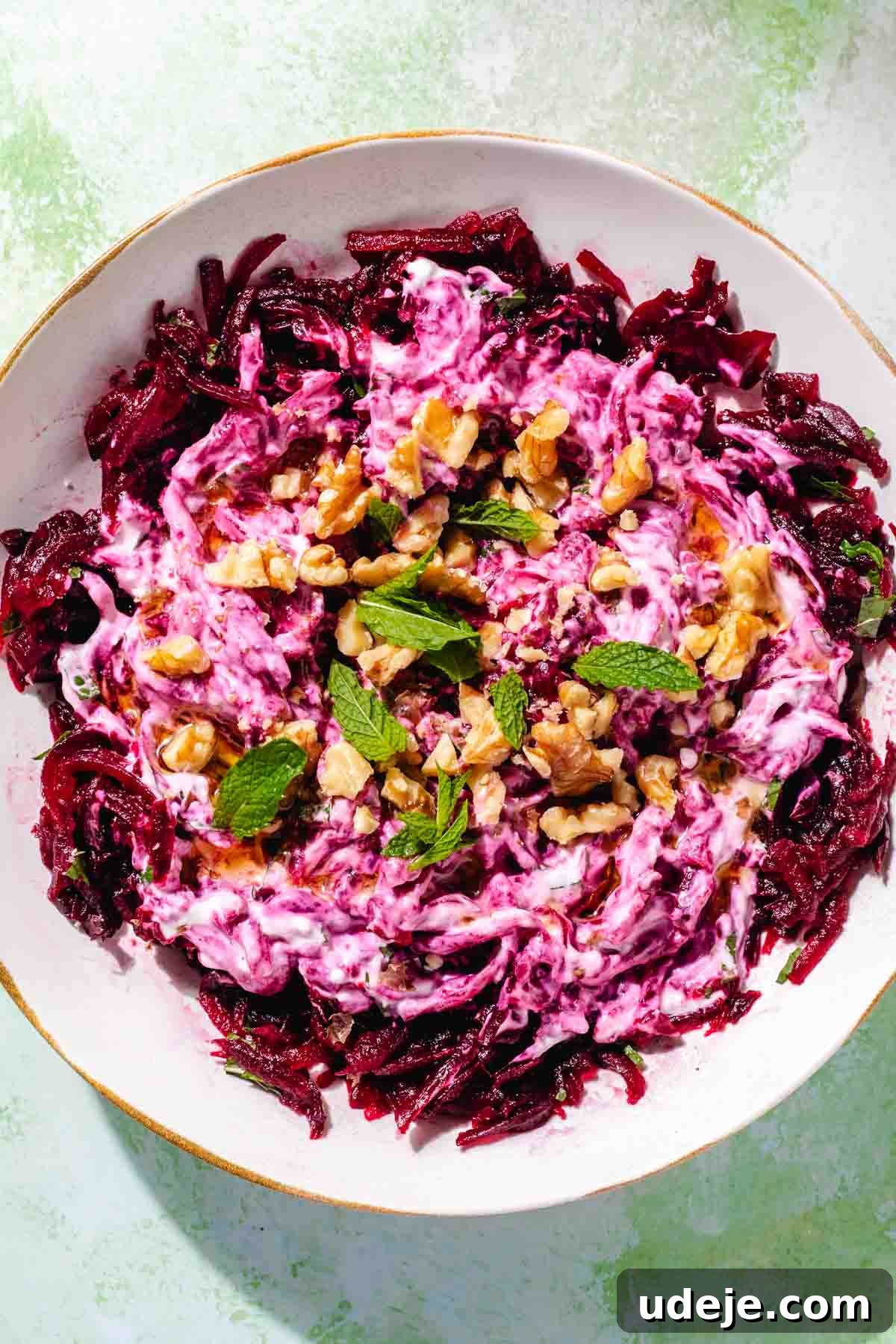 Vibrant Beetroot Yogurt Salad 8 Turkish beet salad garnished with walnuts and mint in a white salad bowl on a green background