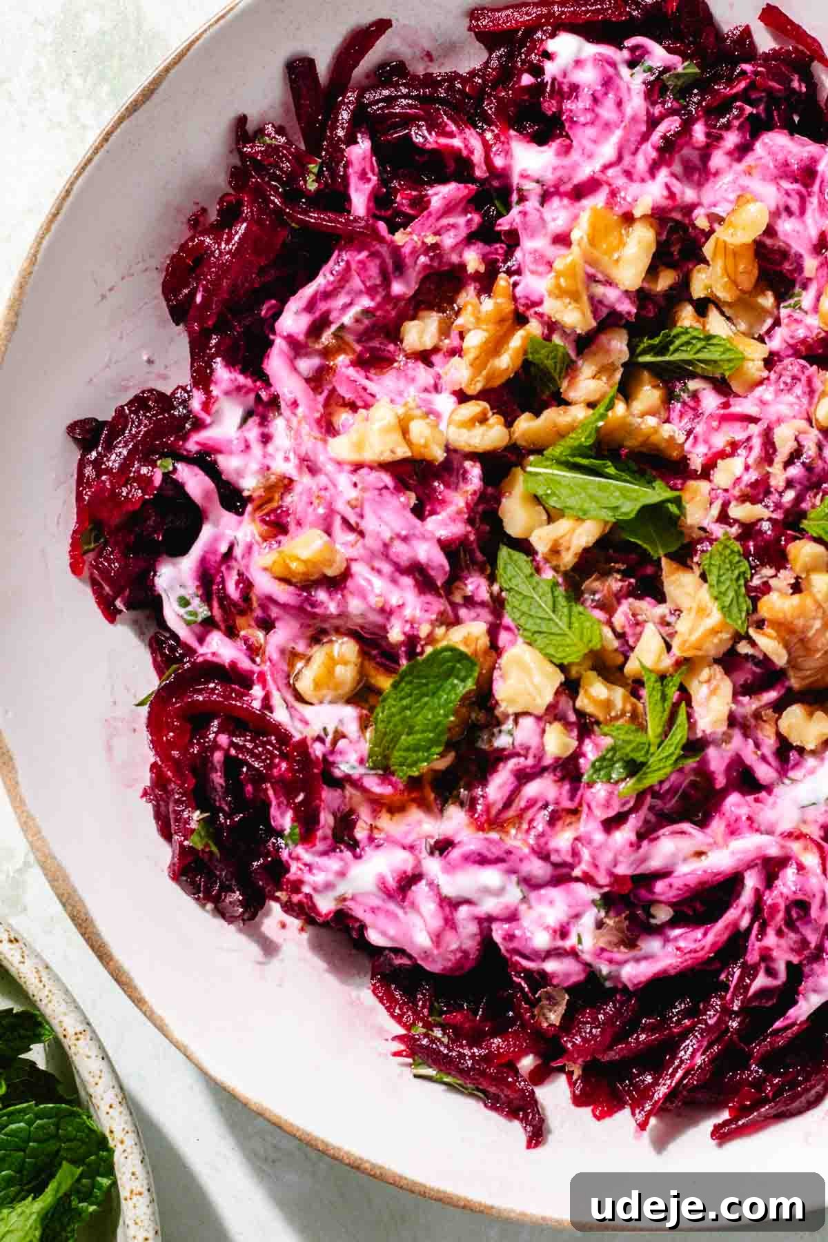 Vibrant Beetroot Yogurt Salad 9 Turkish beet salad garnished with walnuts and mint in a white salad bowl on a green background