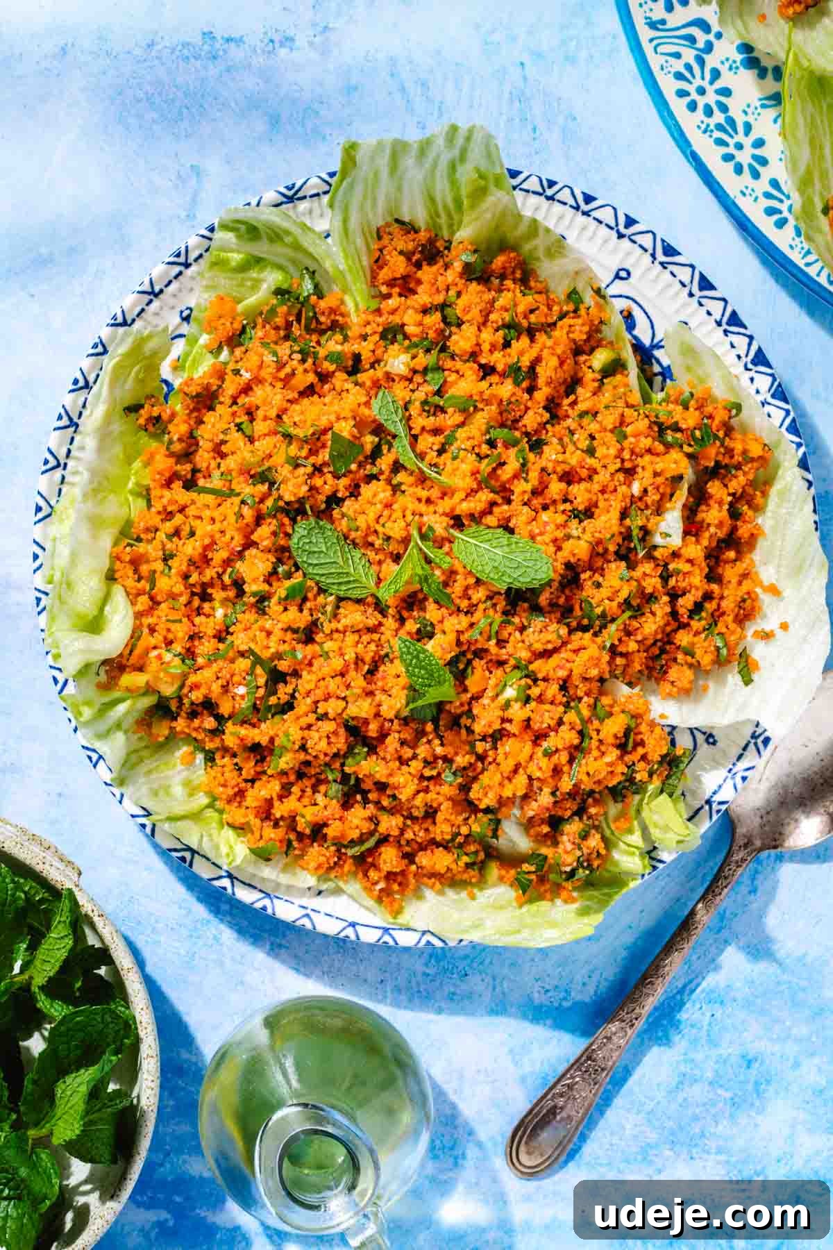 Fast 20-Minute Turkish Bulgur Kisir 2 Vibrant Turkish Kisir salad served on crisp lettuce leaves, garnished with fresh mint, on a beautiful blue and white patterned plate with a spoon, accompanied by a small bowl of mint and a pitcher of olive oil.