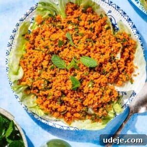 Kisir served over lettuce leaves and garnished with mint on a blue and white patterned plate with a spoon at the side, a bowl of mint leaves and a small pitcher of olive oil