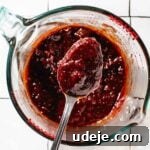 Dressing for kisir mixed together in a glass measuring cup with a spoon being held up with dressing in it on a white tiled surface