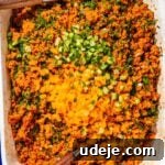 Kisir with chopped cucumbers and peppers on top in a white, blue rimmed baking tray with two wooden servers on the sides