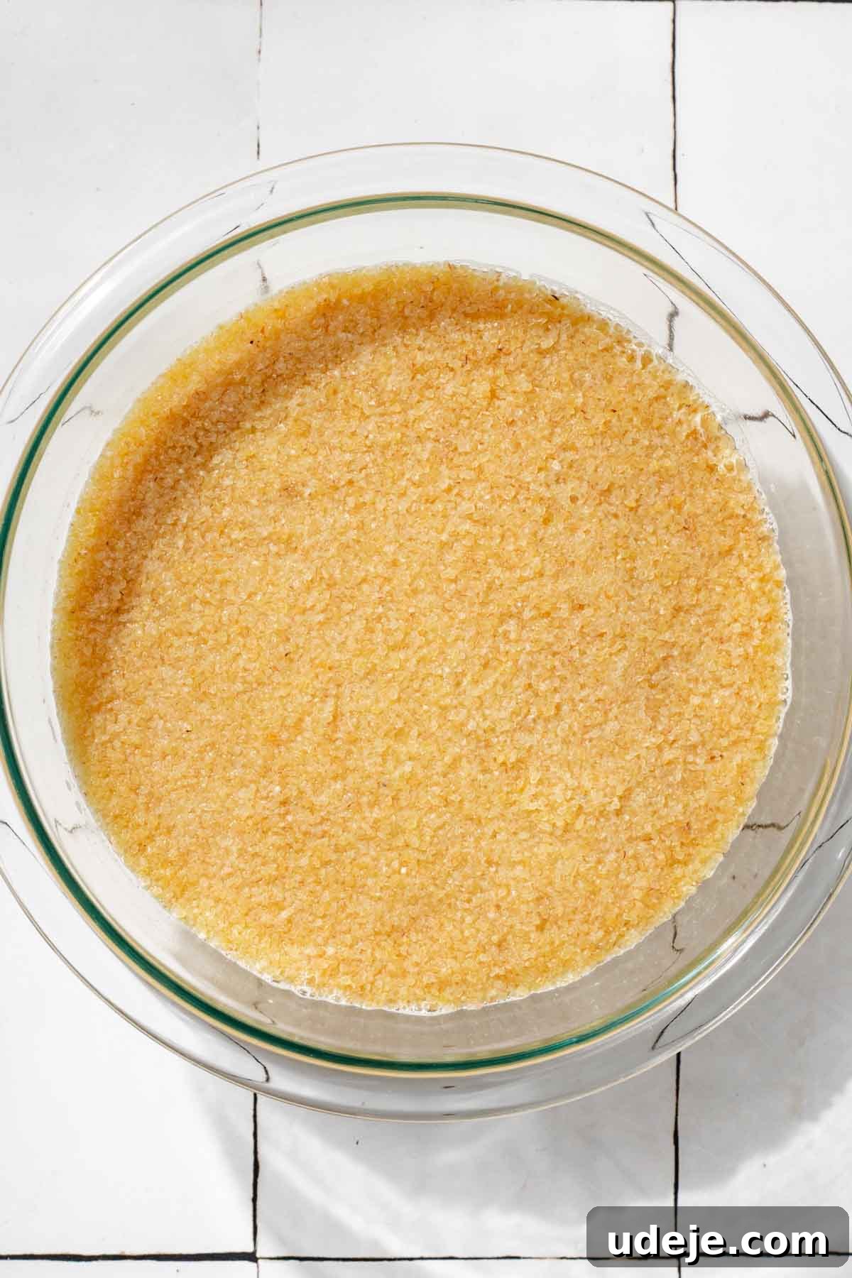 Fast 20-Minute Turkish Bulgur Kisir 6 Fine bulgur grains gently soaking in a clear glass bowl, resting on a clean white tiled surface, illustrating the initial step of softening the bulgur.