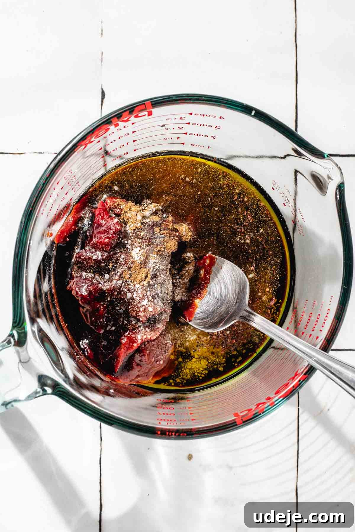Fast 20-Minute Turkish Bulgur Kisir 7 Unmixed ingredients for Kisir dressing in a glass measuring cup: olive oil, pomegranate molasses, tomato paste, red pepper paste, and various seasonings, all neatly arranged on a white tiled surface.