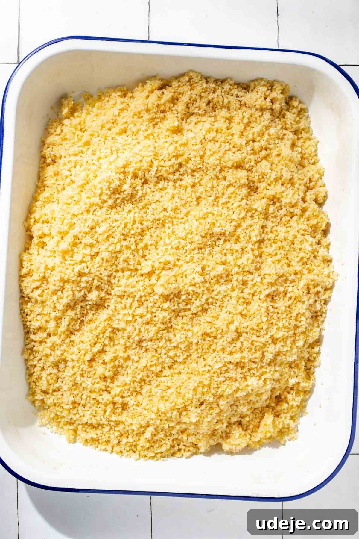 Fast 20-Minute Turkish Bulgur Kisir 10 Perfectly soaked and fluffed bulgur, now ready for dressing, spread evenly in a white baking pan with a subtle blue rim, resting on a white tiled surface.