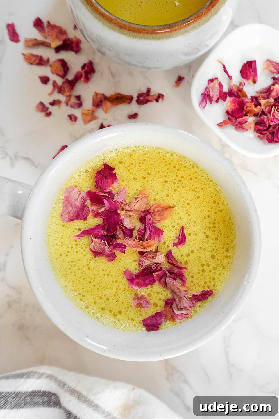 Golden Wellness Elixir 3 A second view of a cup of golden milk (turmeric latte) with a frothy, creamy texture, garnished with rose petals on a marble surface, emphasizing its comforting appeal.