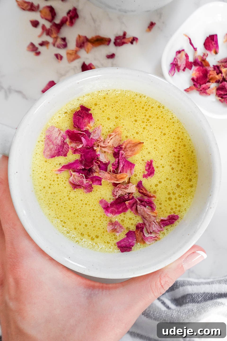 Golden Wellness Elixir 4 A third captivating image of a cup of golden milk (turmeric latte) with its signature frothy texture, adorned with rose petals on a serene marble surface, highlighting its artisanal presentation.