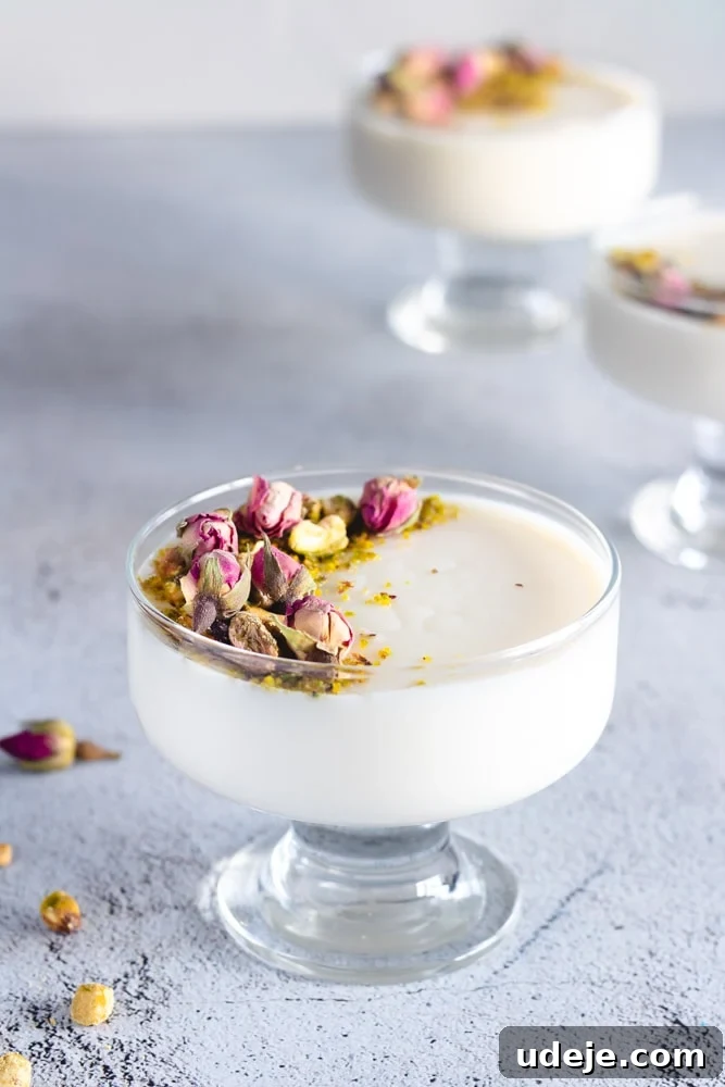 Mahalabia Silky Smooth Middle Eastern Pudding 3 Two serving cups of Mahalabia, adorned with pistachios and dried rosebuds, resting on a pink tray, ready to be enjoyed as a light and fragrant dessert.