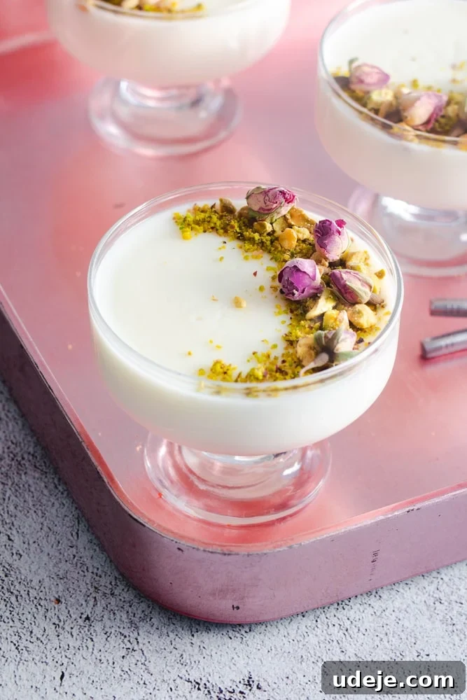 Mahalabia Silky Smooth Middle Eastern Pudding 4 Close-up of a serving cup of Mahalabia (or Muhallebi) Milk Pudding, meticulously garnished with chopped pistachios and delicate rosebuds, showcasing a rich, creamy texture.