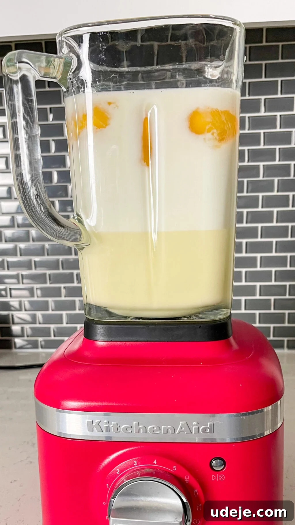 Creamy Condensed Milk Creme Caramel 12 creme caramel mixture in glass blender with red bottom and grey tiled backsplash