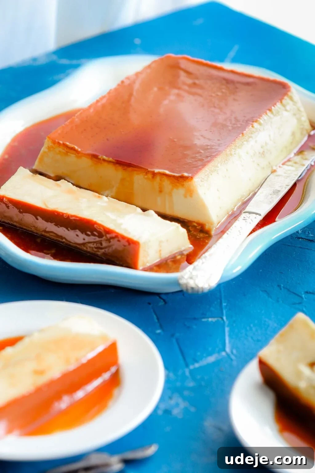 Creamy Condensed Milk Creme Caramel 18 front view of sliced creme caramel with knife beside it on a blue rimmed dish with 2 slices of creme caramel on plates on a blue background