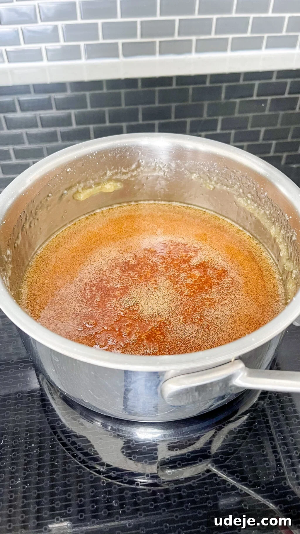 Creamy Condensed Milk Creme Caramel 8 deep golden simmering caramel in a steel saucepan on a dark coloured stovetop