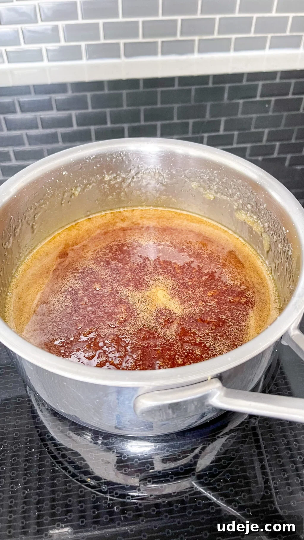 Creamy Condensed Milk Creme Caramel 9 deep golden simmering caramel in a steel saucepan on a dark coloured stovetop