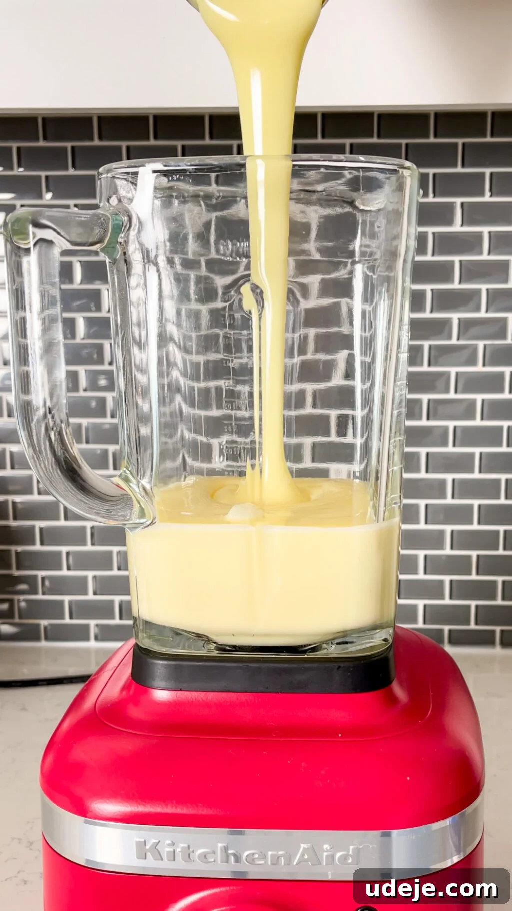 Creamy Condensed Milk Creme Caramel 10 condensed milk pouring into a glass blender jug on a red bottom with a dark grey tiled backsplash