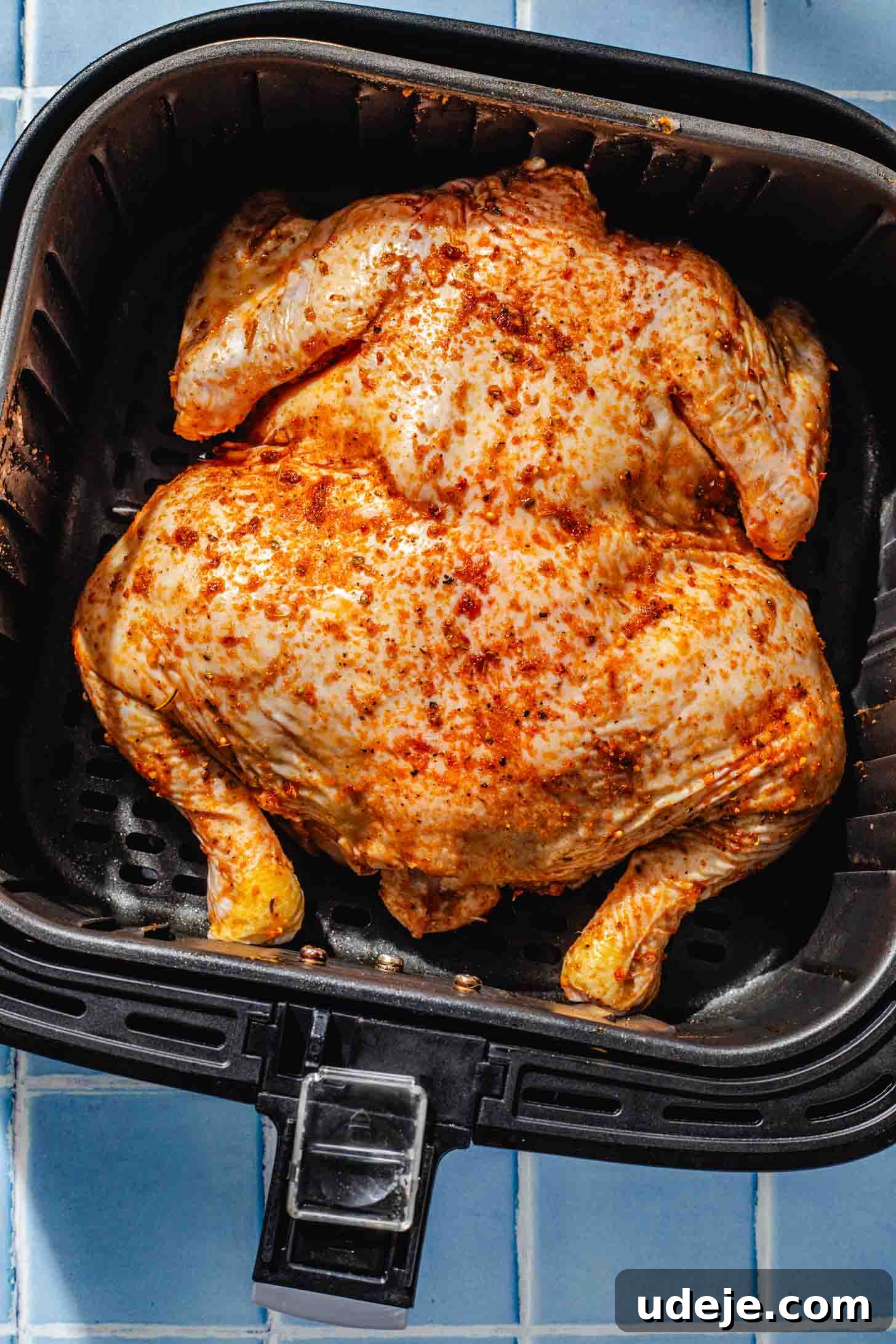 Crispy and Juicy Air Fryer Whole Chicken in 60 Minutes 6 whole marinated chicken in a black airfryer basket on a blue tiled background