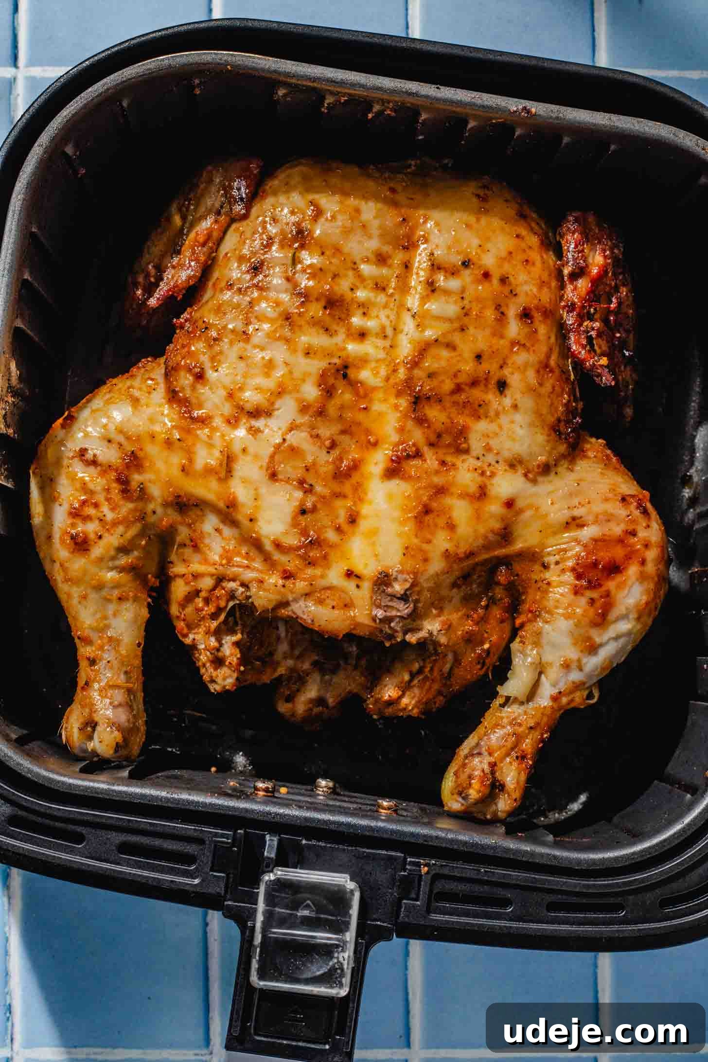 Crispy and Juicy Air Fryer Whole Chicken in 60 Minutes 7 half cooked whole marinated chicken in a black airfryer basket on a blue tiled background