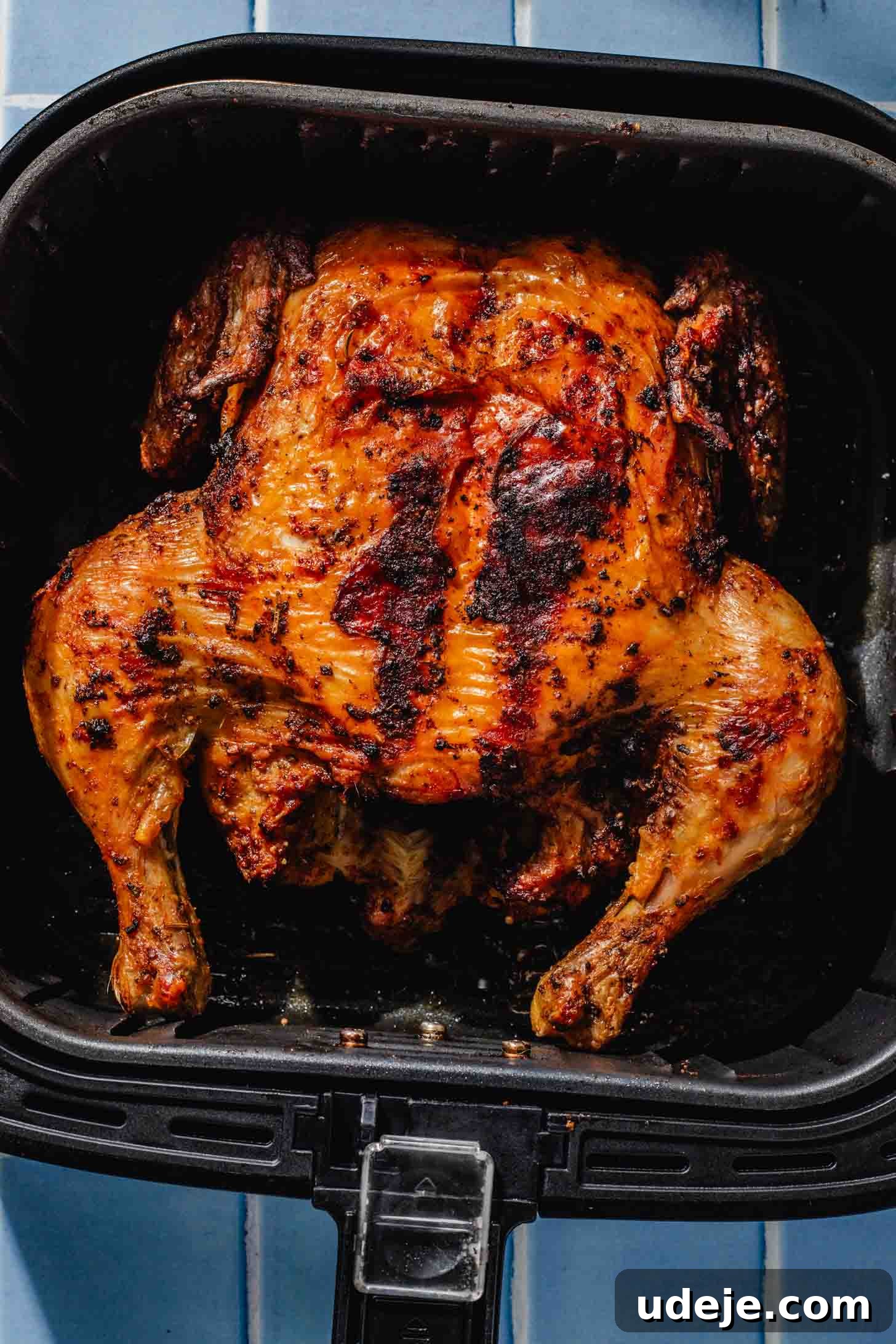 Crispy and Juicy Air Fryer Whole Chicken in 60 Minutes 8 air fried whole chicken in a black air fryer basket on a blue tiled background