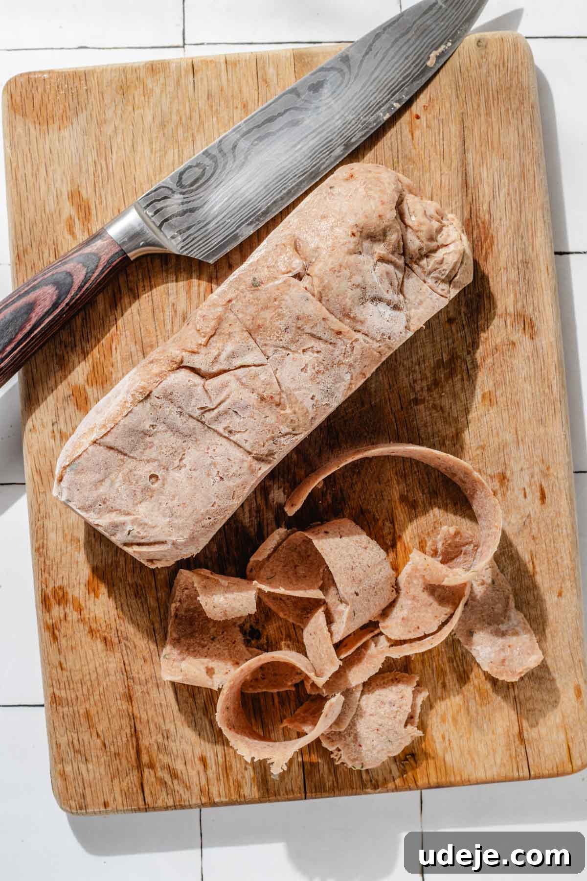 One-Pan Lamb and Beef Doner Kebab 15 A sharp, large knife is meticulously slicing a frozen doner log into delicate, thin strips on a robust wooden cutting board, preparing the meat for cooking.